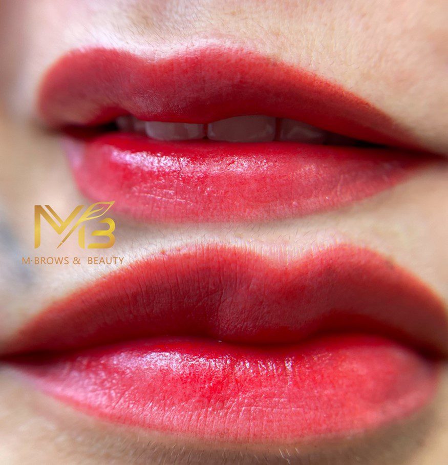 M Brows and Beauty Close-up of a person's lips with bright red lip tint and a soft gradient effect. The skin appears smooth, and the logo "M Brows & Beauty" is visible on the left side of the image.