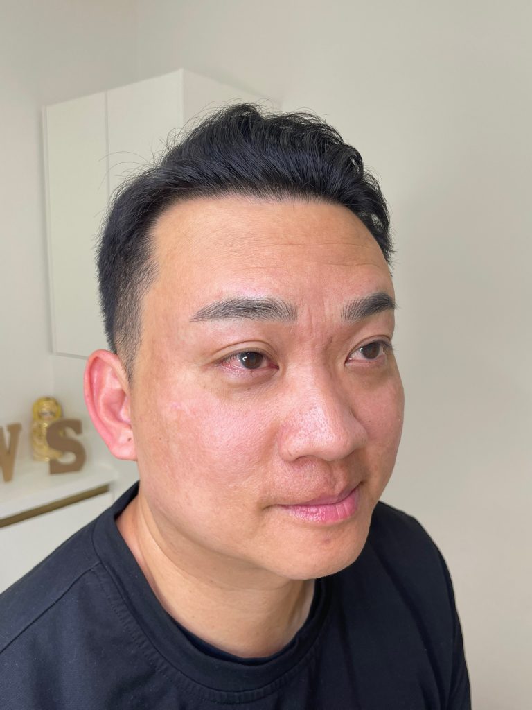 M Brows and Beauty A man with short black hair and a trimmed beard is wearing a black shirt and looking slightly to the side in a well-lit room with white walls and cupboards—perfect lighting for showcasing cosmetic tattoo Sydney results.