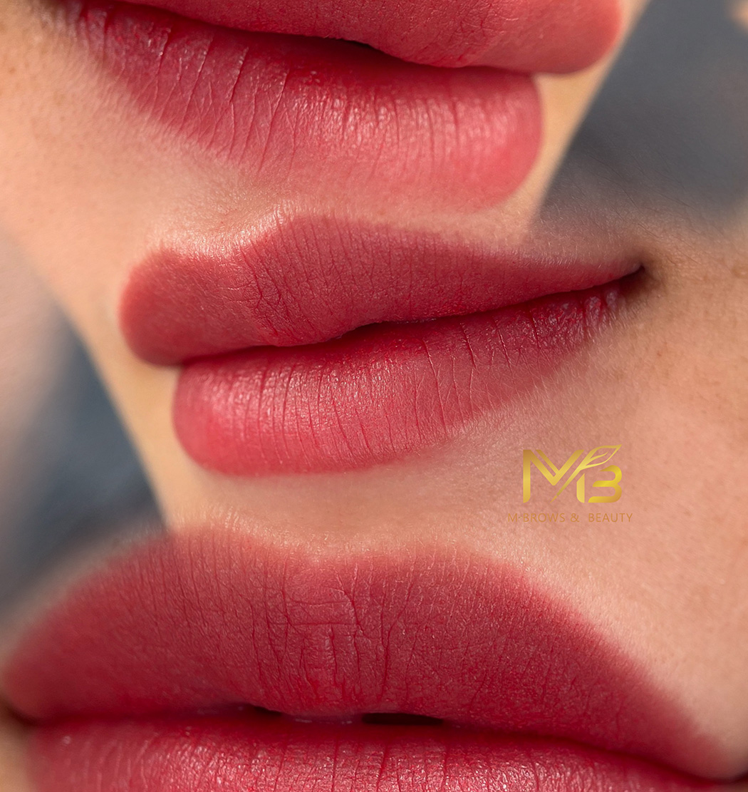 M Brows and Beauty Close-up collage of lips with smooth, natural pinkish-red lipstick, shown from different angles. The softly blurred background highlights a subtle gold logo reading "MB Brows & Beauty," specialists in cosmetic tattoo Sydney.
